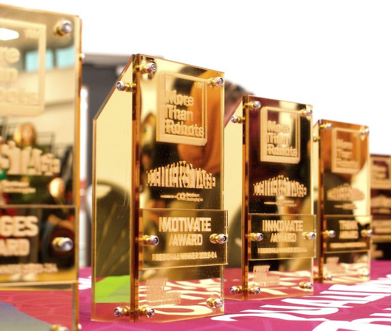 A row of gold trophies sitting on a table covered in fabric with a pull up banner in the background